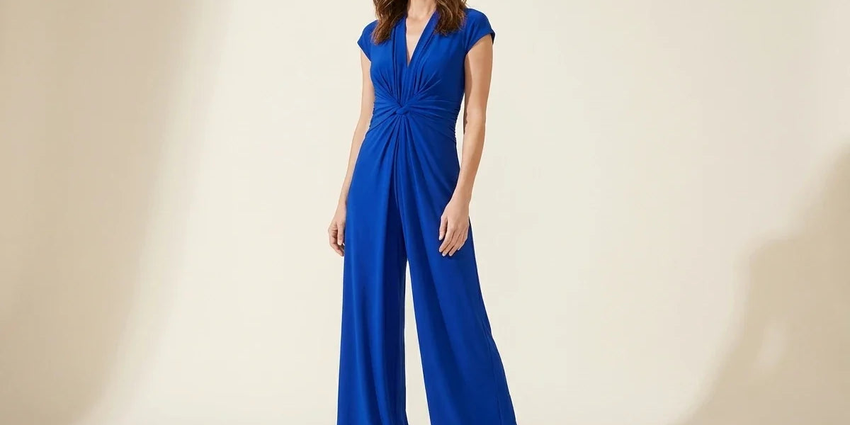 Brunette woman modeling a Vince Camuto royal blue cap-sleeve wide-leg jumpsuit with a twisted knot waist and nude heels.