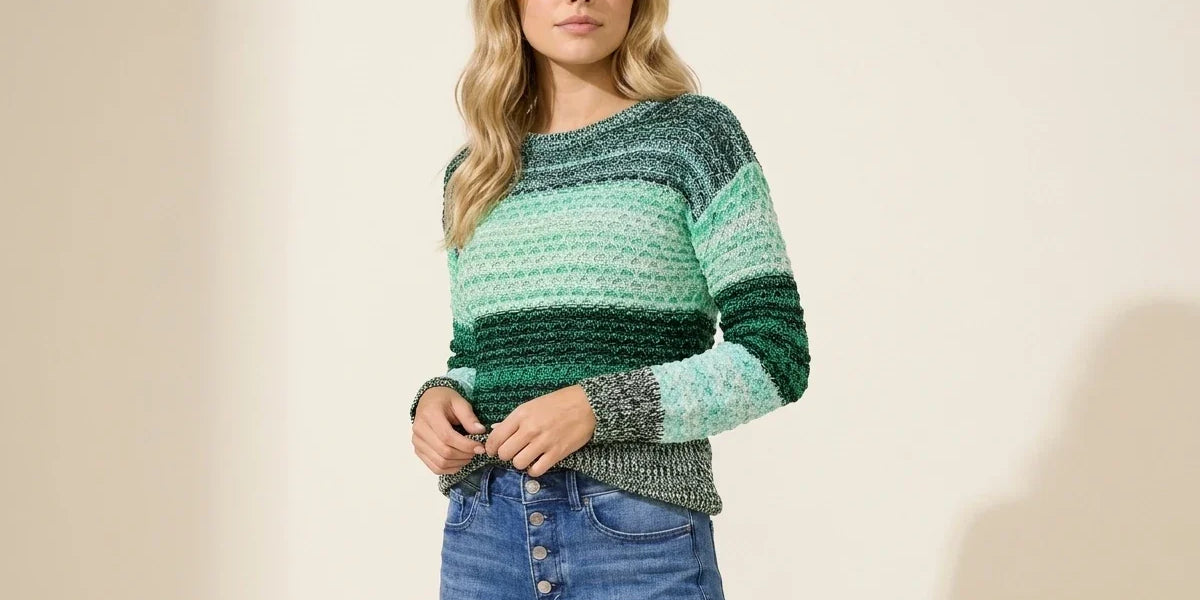 Blonde woman modeling a Vince Camuto textured crewneck sweater in green, mint, and forest ombre stripes paired with medium-wash jeans.