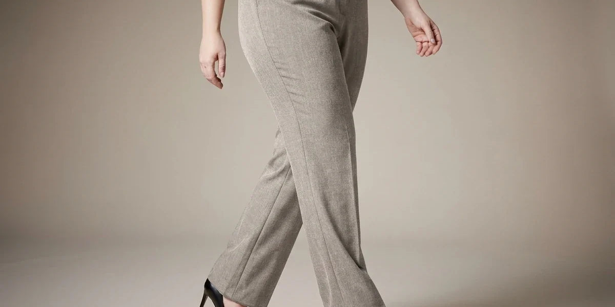 A model wearing light beige straight-leg trousers, a white long-sleeve blouse, and black high heels, shown from the waist down against a neutral beige studio background.