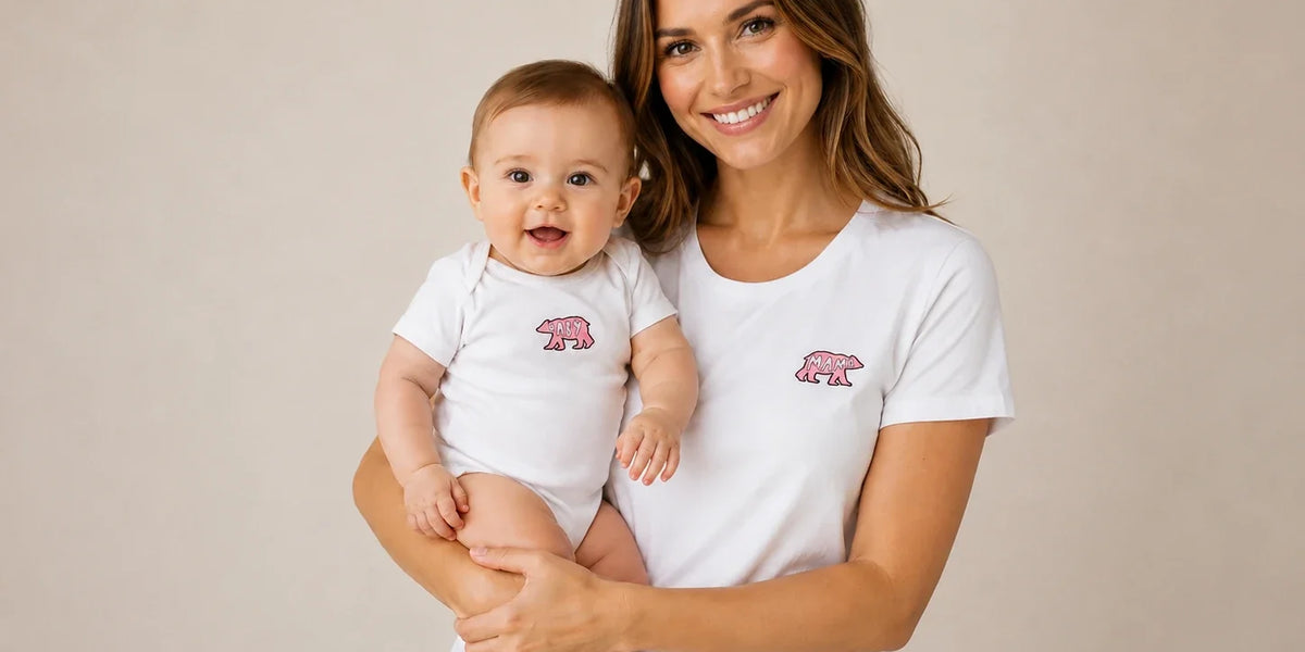 Mother holding her smiling baby wearing matching white shirts with pink 'Mama Bear' and 'Baby Bear' graphics.