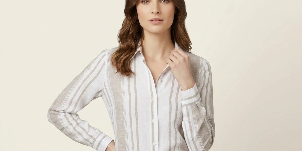 Brunette woman modeling a white and beige vertical-striped button-up linen blouse tucked into grey plaid trousers against a neutral background.