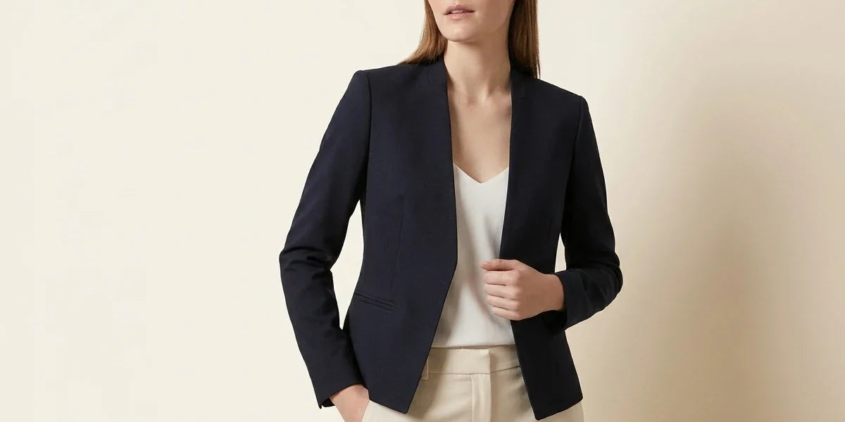 Blonde woman modeling a Calvin Klein navy blue collarless open-front tailored blazer over a white top and cream dress pants.