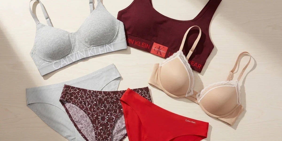 Flat-lay collection of Calvin Klein women's bras, bralettes, and panties in grey, burgundy, beige lace, and red on a neutral surface.