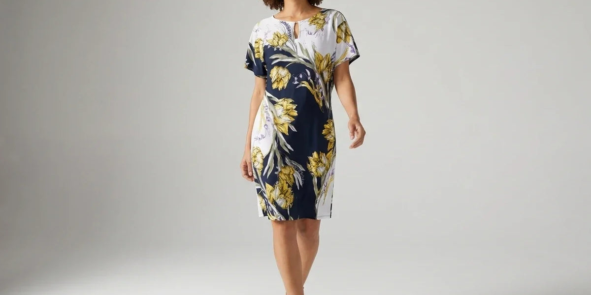 A woman modeling a short-sleeve knee-length dress with a navy blue, white, and yellow floral print, standing against a light gray studio background.