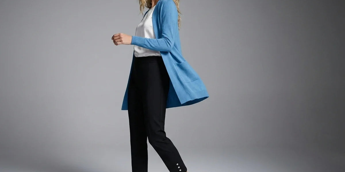 A woman modeling a light blue open-front cardigan over a white top and black cropped pants, standing against a neutral gray studio background.
