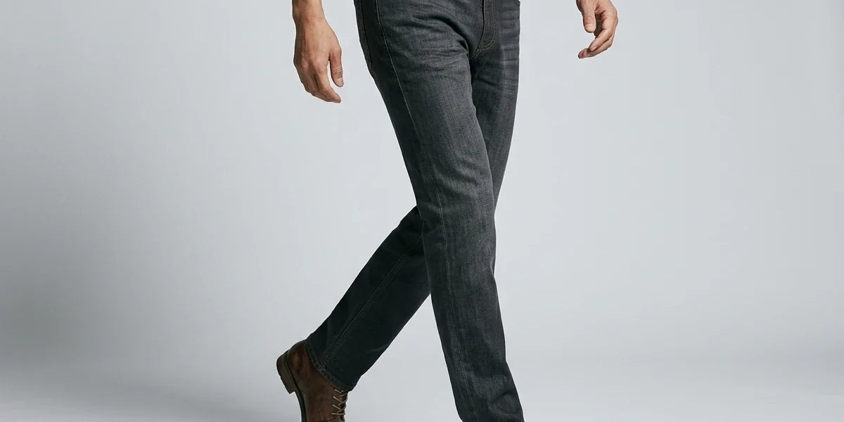 Side profile of a man walking wearing dark grey slim-straight jeans, a brown leather belt, and brown lace-up boots.