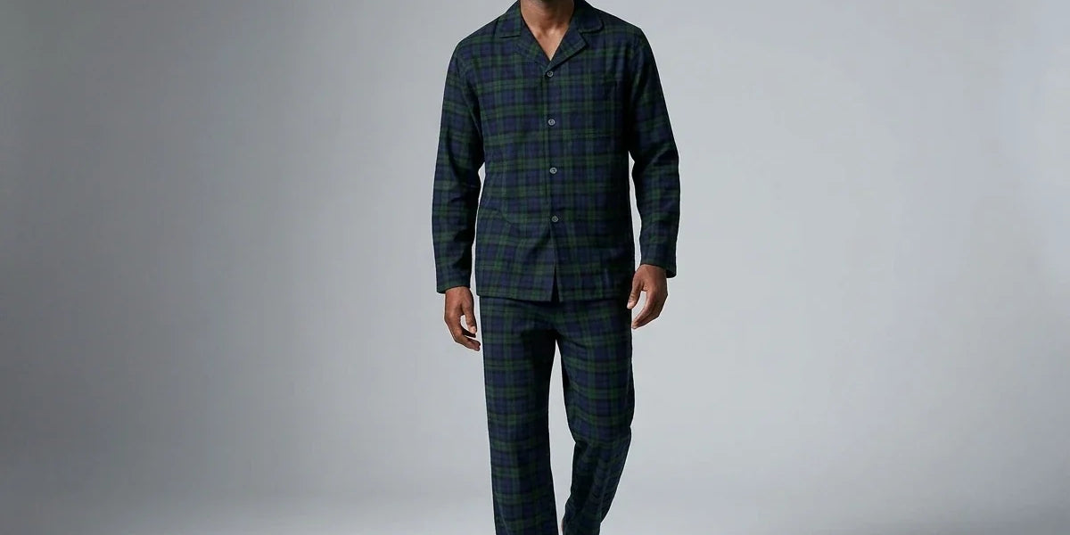 A man modeling a two-piece long-sleeve pajama set with a dark green and black plaid pattern, walking against a neutral gray studio background.