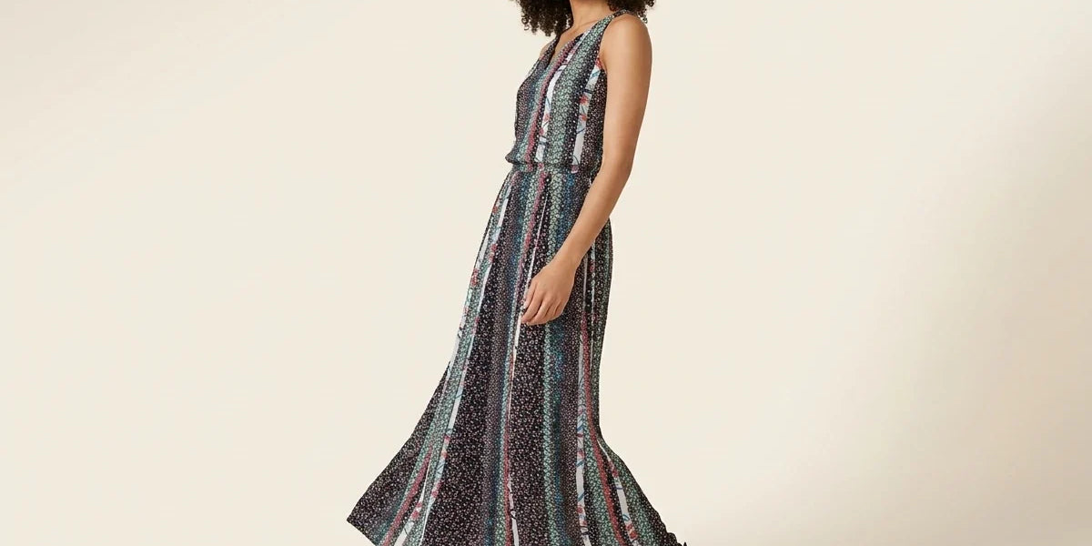 Woman with curly brown hair modeling a sleeveless floral and vertical stripe maxi dress paired with black strappy flat sandals.