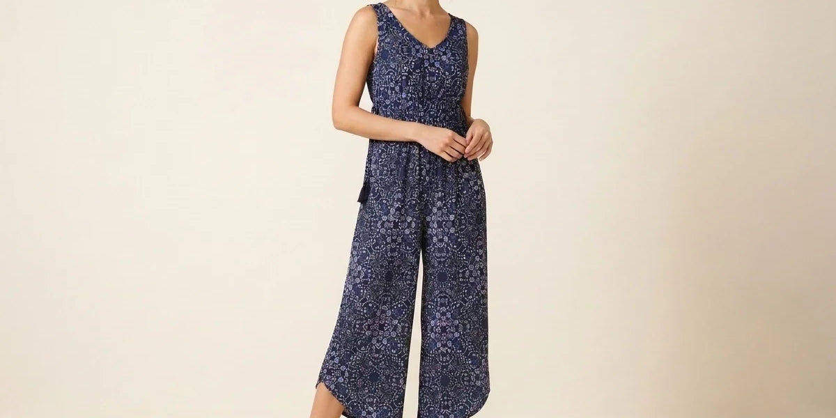 Brunette woman modeling a sleeveless navy blue floral print wide-leg cropped jumpsuit paired with brown strappy gladiator flat sandals.