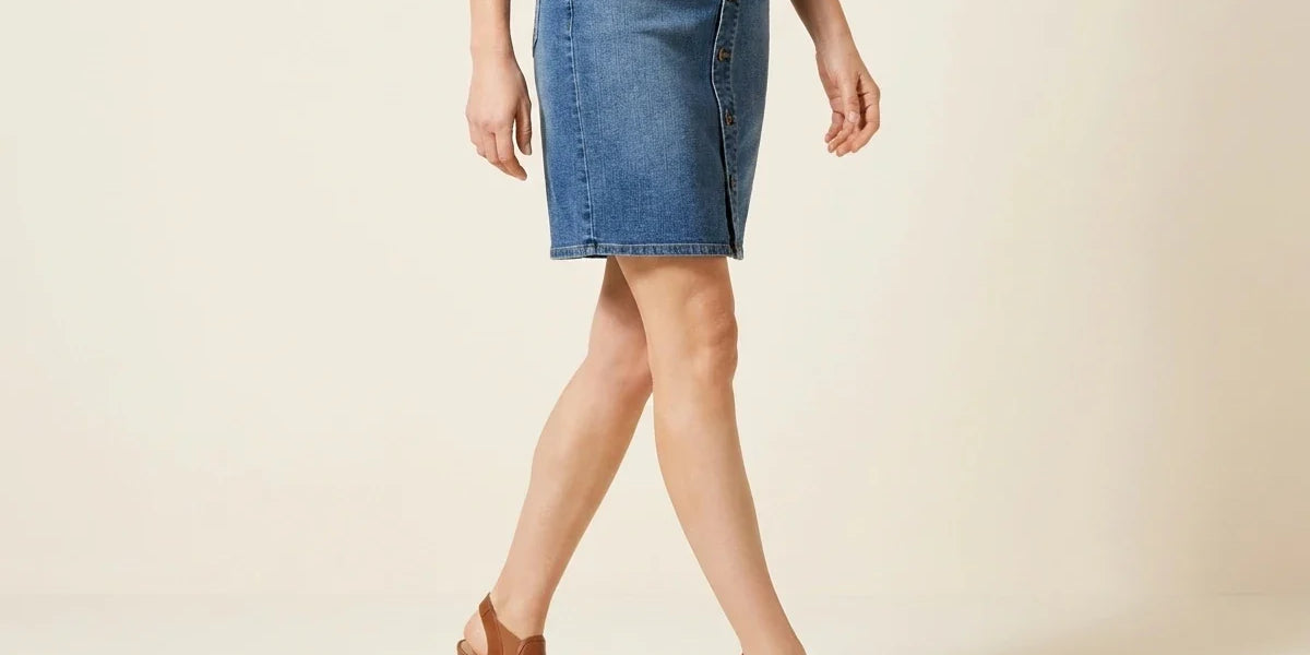 Cropped view of a woman wearing a petite button-front medium wash denim mini skirt with brown open-toe wedge sandals.