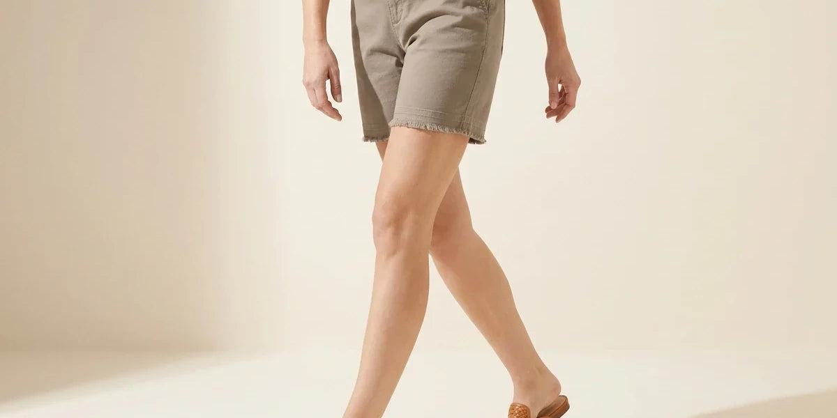 Cropped view of a woman wearing petite taupe khaki stretch shorts with raw fray hem and cognac woven leather mule flats.