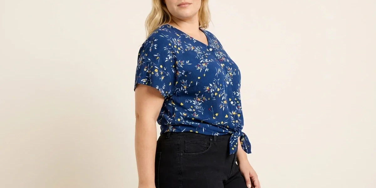 Blonde woman modeling a plus-size cobalt blue floral short-sleeve top with a side-tie knot hem paired with black jeans.