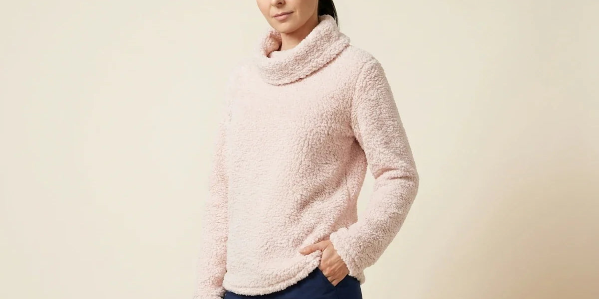Brunette woman modeling a petite blush pink fuzzy sherpa fleece cowl-neck sweater paired with navy blue pants.
