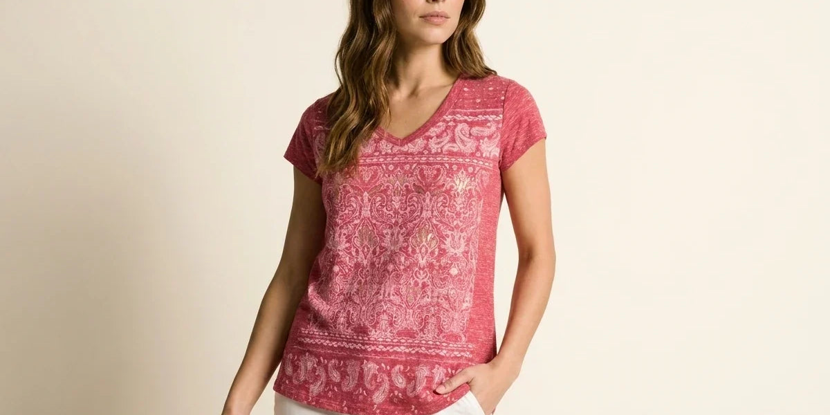 Brunette woman modeling a raspberry pink short-sleeve V-neck t-shirt with a paisley tapestry graphic print paired with white pants.