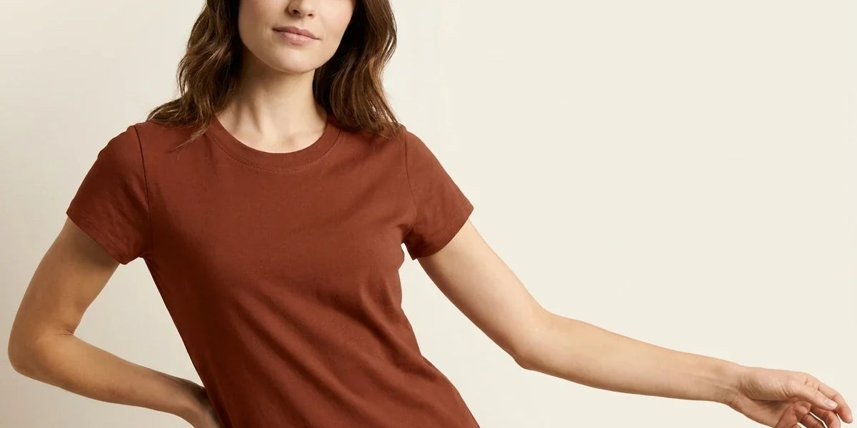 A woman modeling a short-sleeve crewneck t-shirt in a warm rust brown color, posed against a solid light beige background.