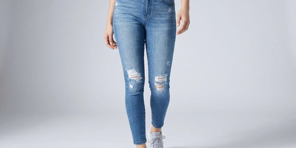A model wearing light blue distressed skinny jeans with ripped details on the thighs and knees, paired with a patterned crop top and gray sneakers, shown against a light gray studio background.