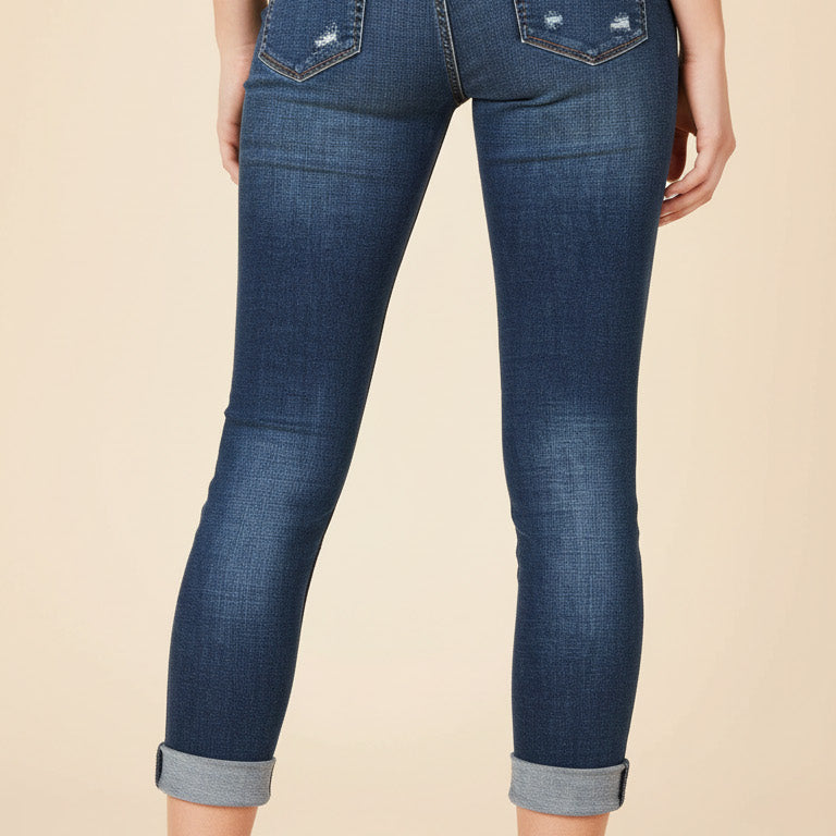 Person wearing blue jeans with rolled-up cuffs on a beige background
