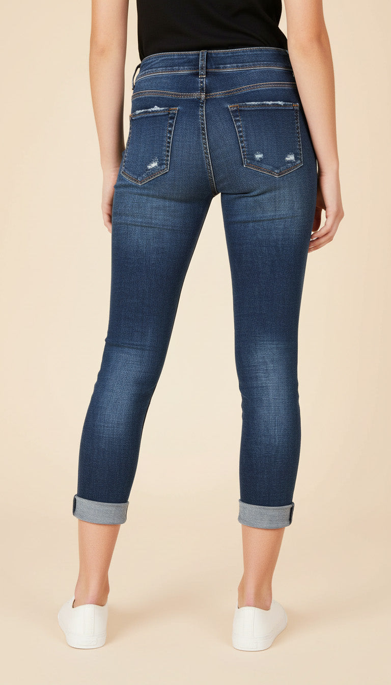 Person wearing blue jeans with rolled-up cuffs on a beige background