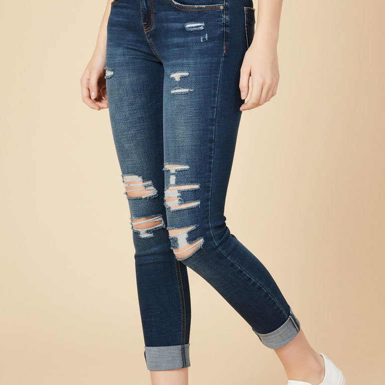 Person wearing distressed blue jeans and white sneakers on a beige background