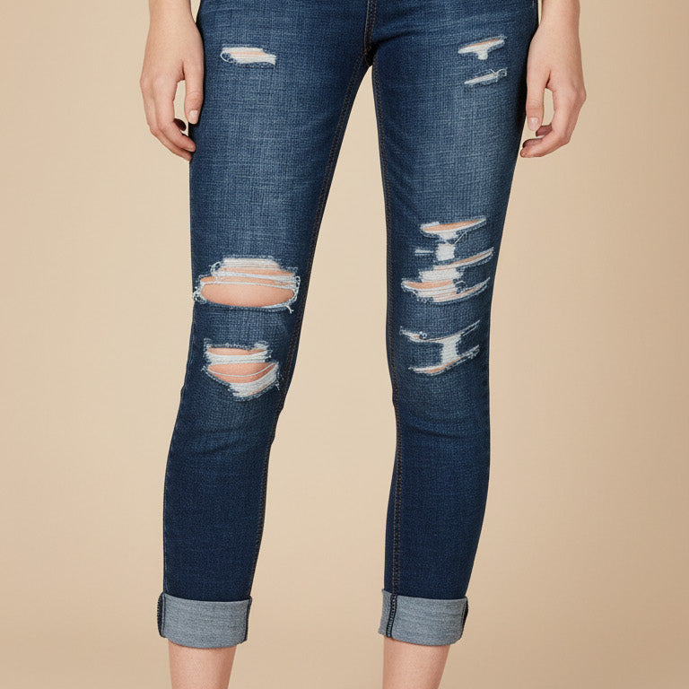 Person wearing distressed blue jeans and white sneakers on a beige background
