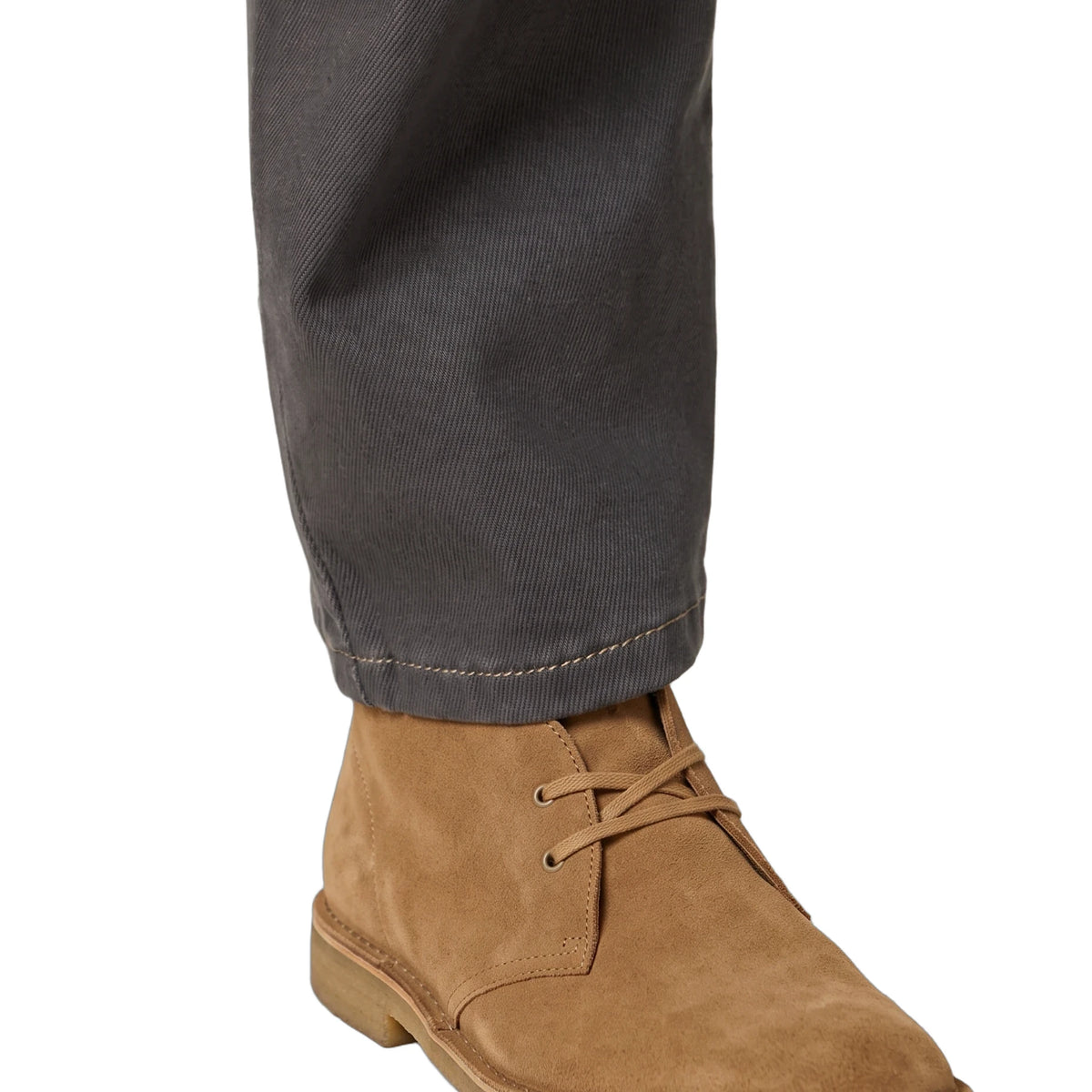 A close-up of a person's foot wearing a tan suede lace-up ankle boot with dark gray trousers, shown against a plain white background.