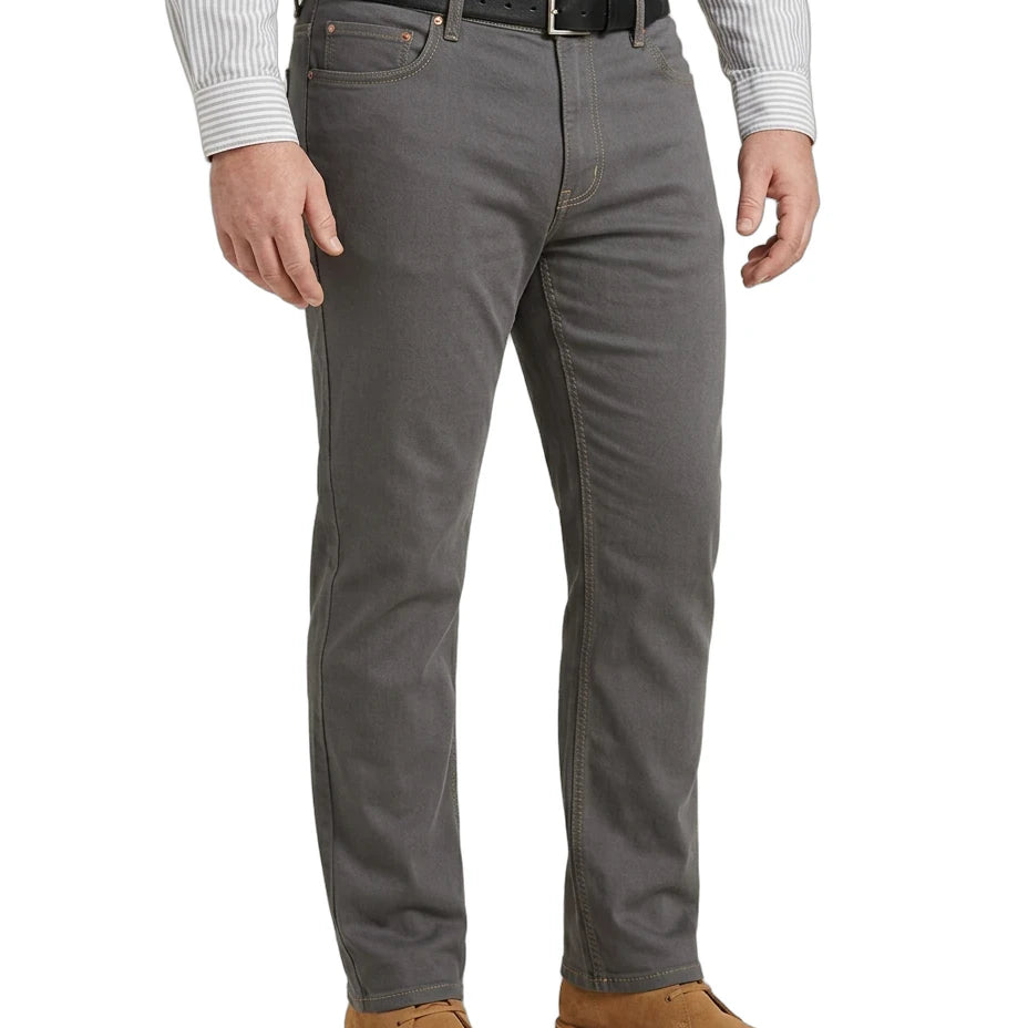 A man wearing gray slim-fit jeans with a black belt, a white striped long-sleeve shirt, and brown suede shoes, shown from the waist down on a white background.