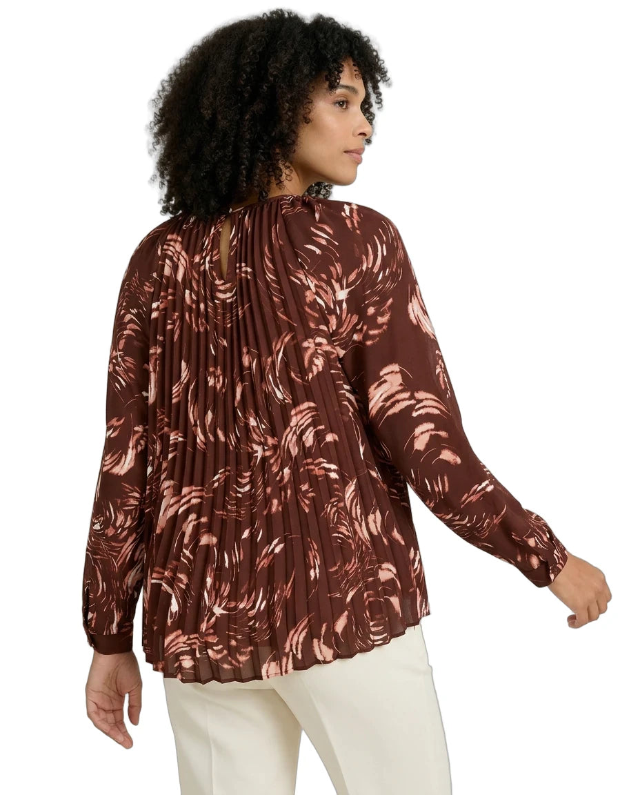 Woman wearing a brown patterned blouse with white pants on a white background