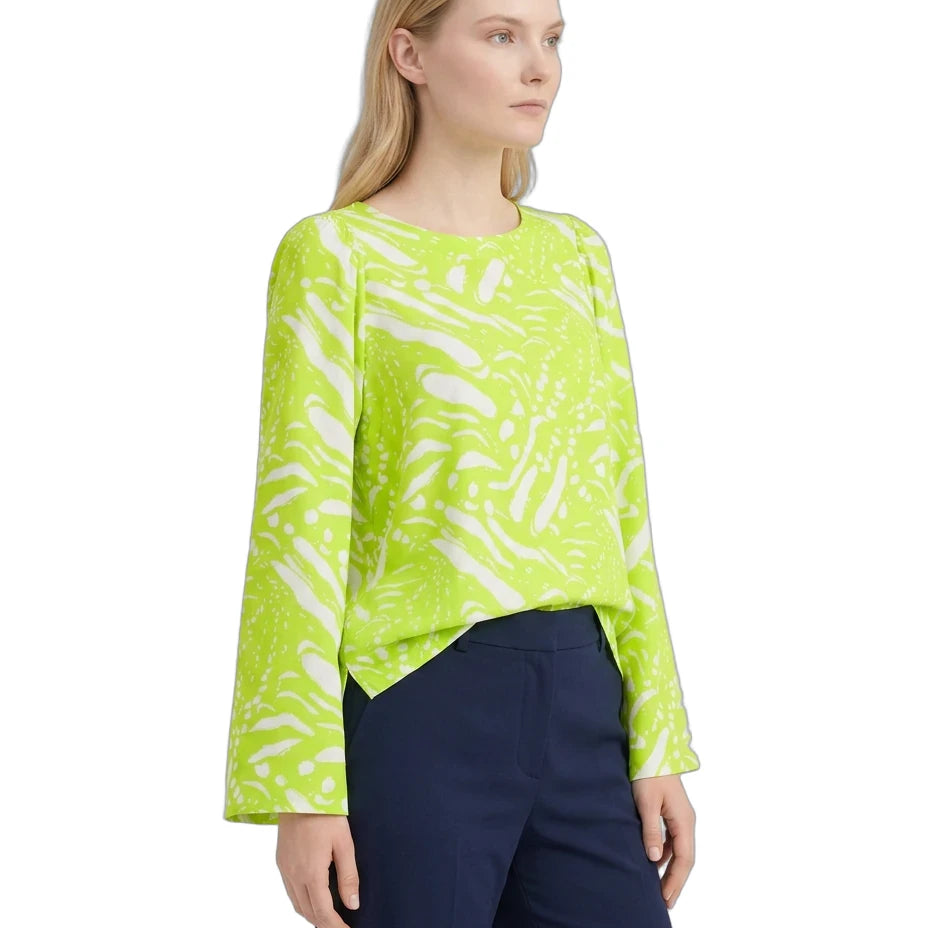 A woman modeling a bright lime green long-sleeve blouse with an abstract white brushstroke pattern, paired with navy blue trousers, against a plain white background.