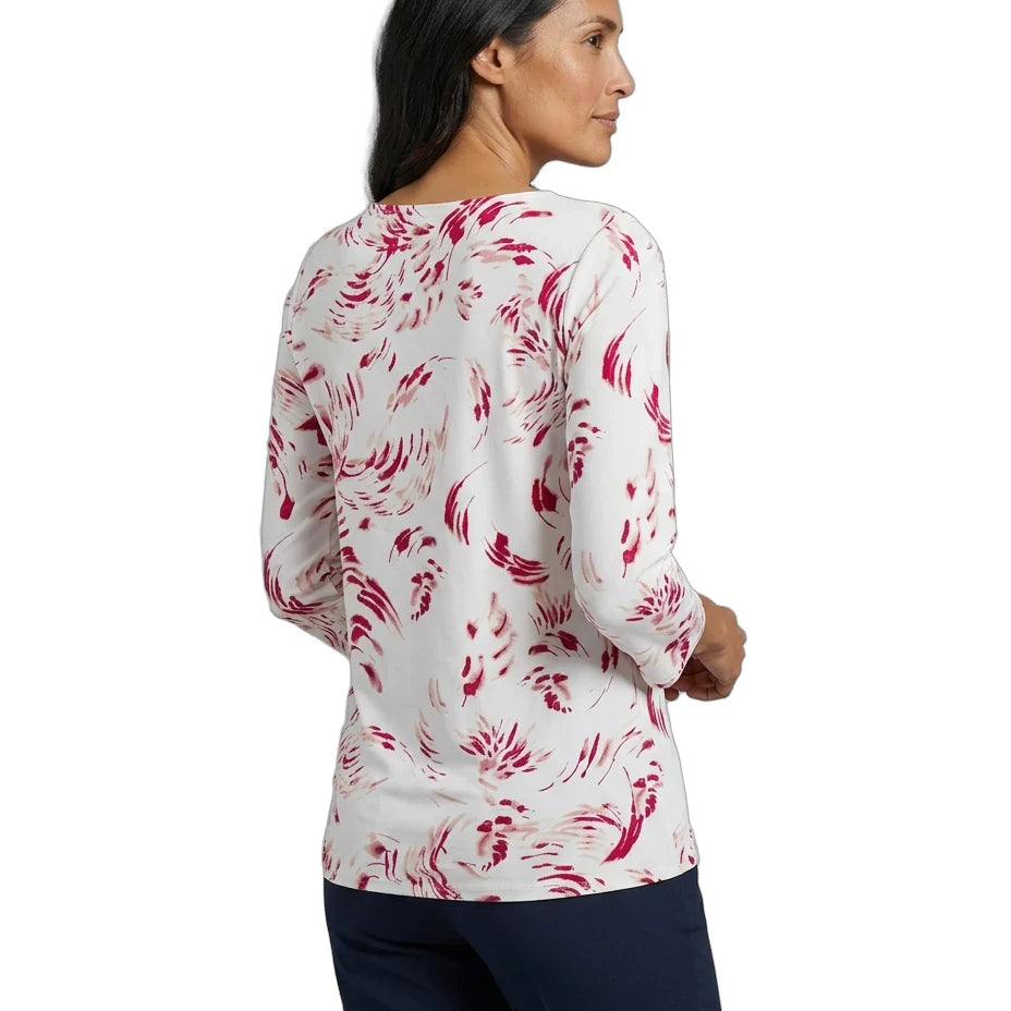 A woman shown from the back wearing a white long-sleeve top with a pink abstract floral pattern, paired with dark navy pants, against a plain white background.