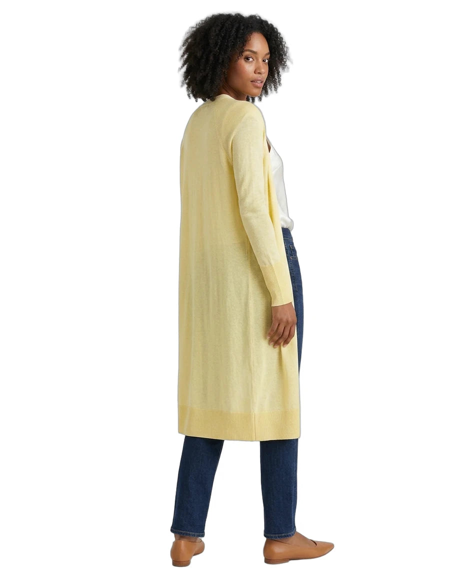 Woman wearing a long light yellow cardigan over a white top and dark pants on a white background