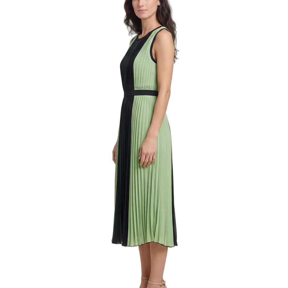 A woman modeling a sleeveless pleated midi dress with a color-blocked design in sage green and black, paired with beige block-heel sandals, against a plain white background.
