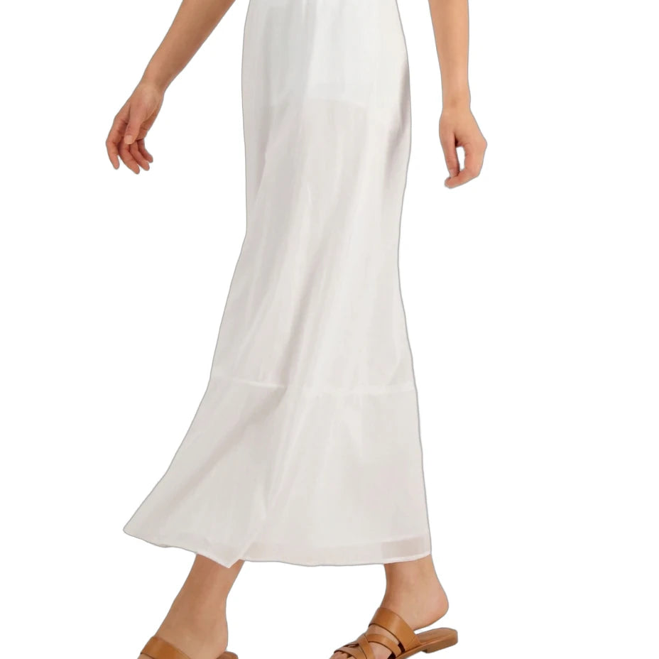 A model wearing a white tiered maxi skirt with a smocked waistband, paired with tan slide sandals, shown against a plain white background.