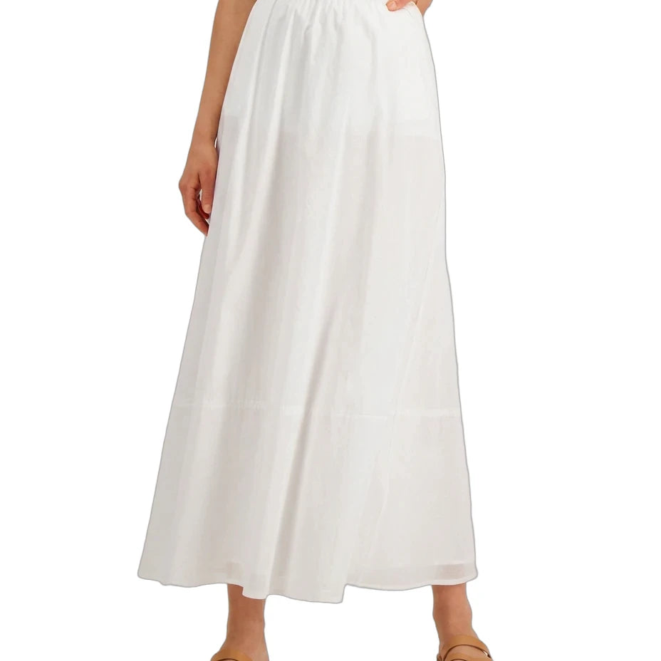 A model wearing a white midi skirt with a smocked waistband, paired with a white top and tan leather sandals, shown against a plain white background.