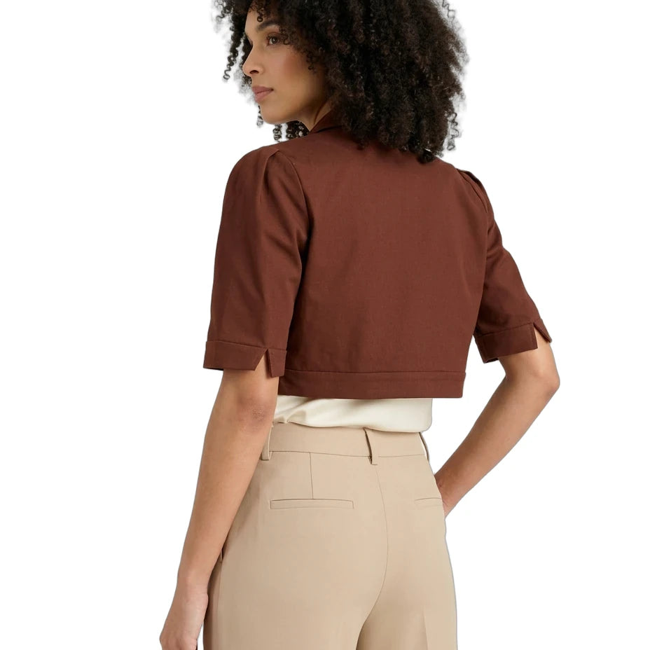 A woman shown from the back wearing a cropped brown short-sleeve top with rolled cuffs, paired with beige trousers and a white undershirt, against a plain white background.