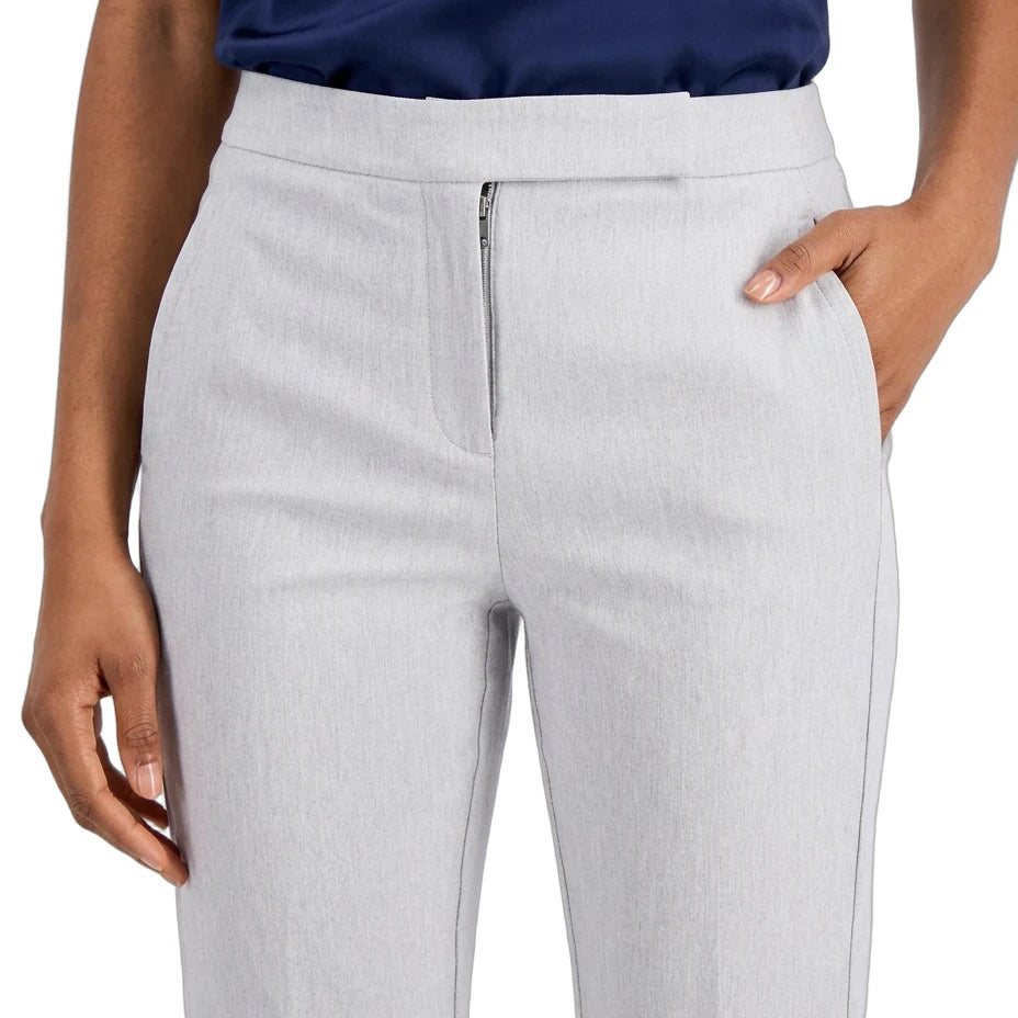 A close-up of a model wearing light gray tailored trousers with a front zipper, paired with a navy top against a plain white background.