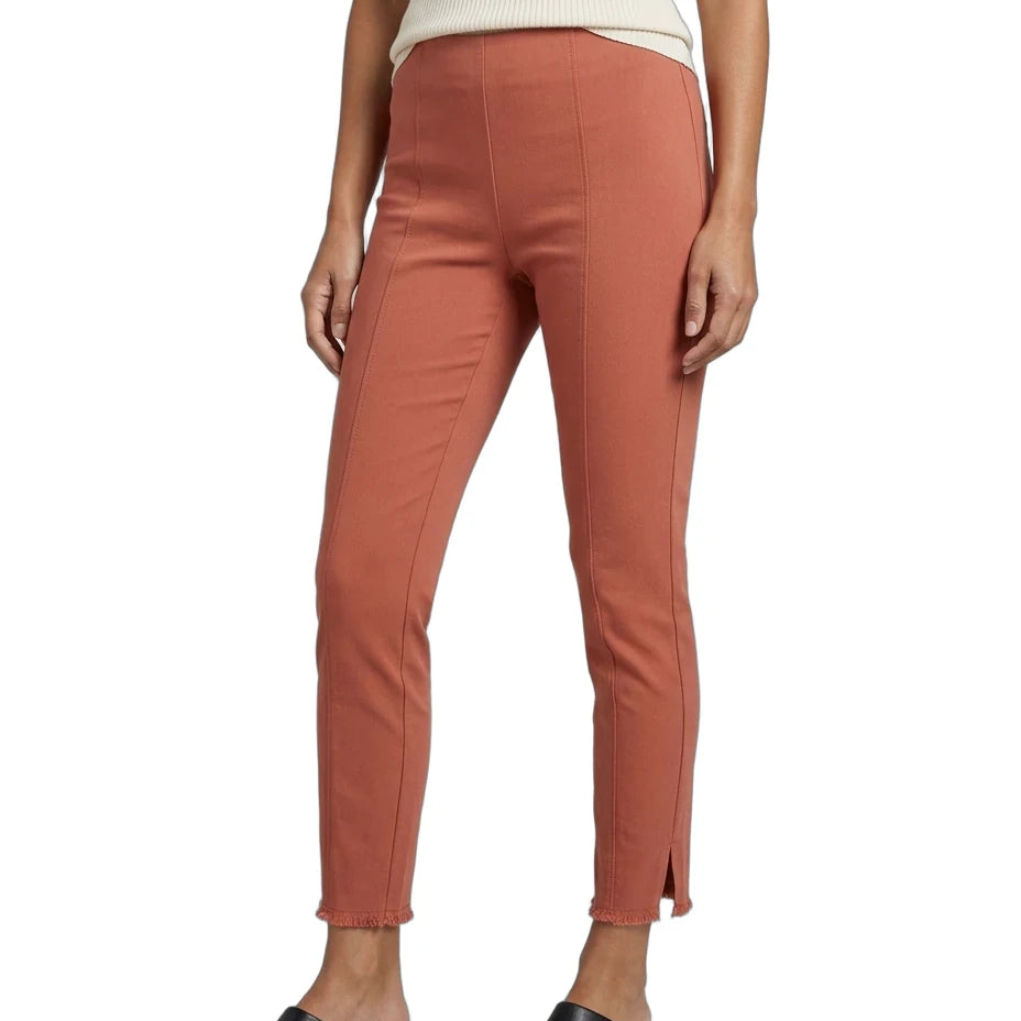 A model wearing slim-fit, ankle-length terracotta pants with side slits, paired with a cream ribbed top and black pointed mule flats, shown against a plain white background.