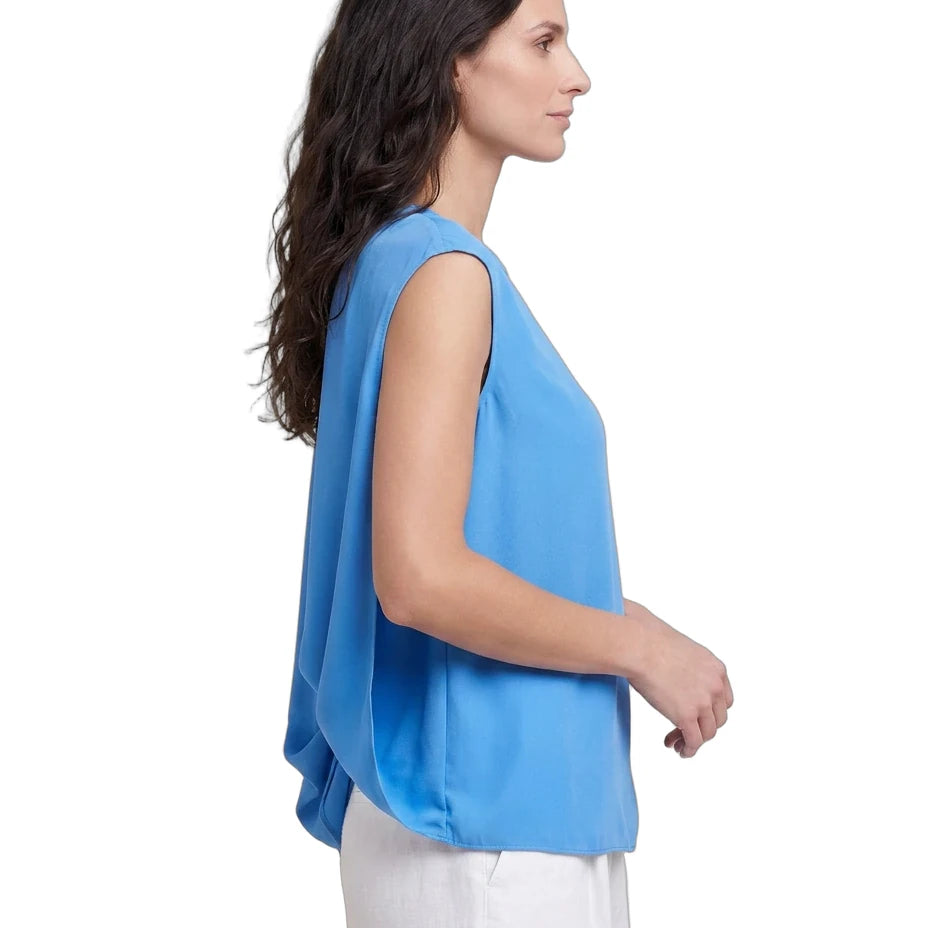 Woman wearing a blue sleeveless top and white pants on a white background