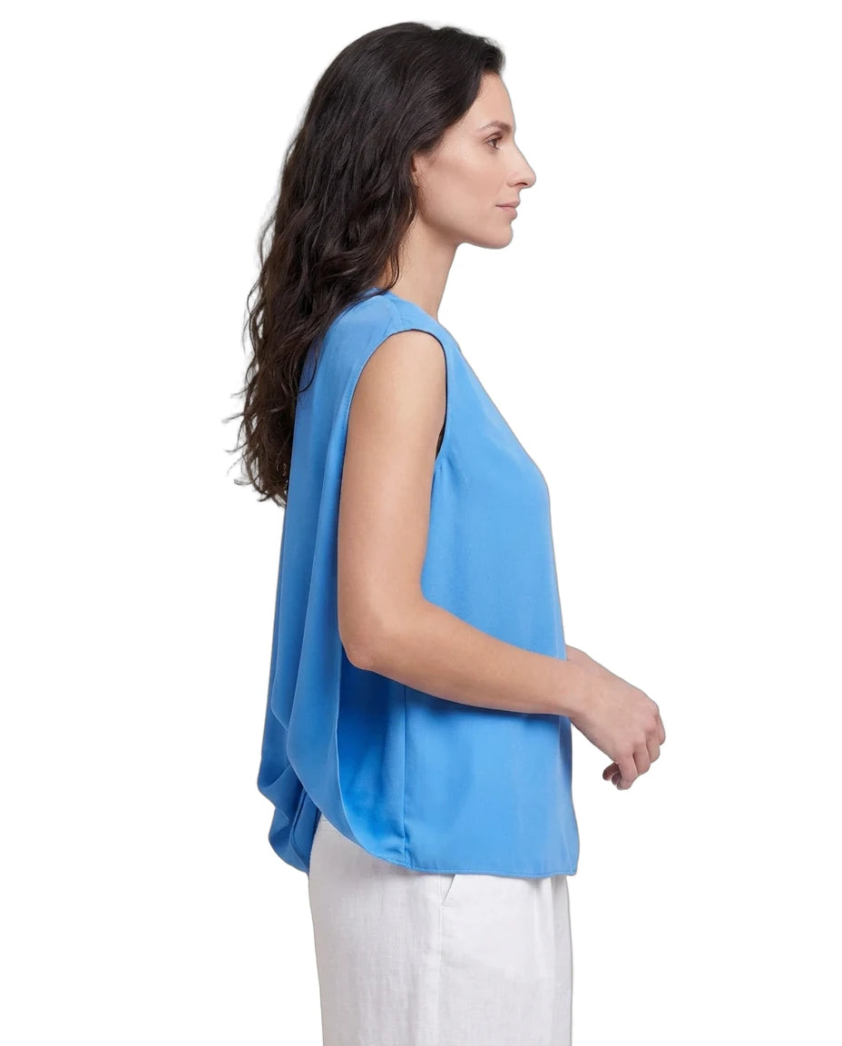 Woman wearing a blue sleeveless top and white pants on a white background