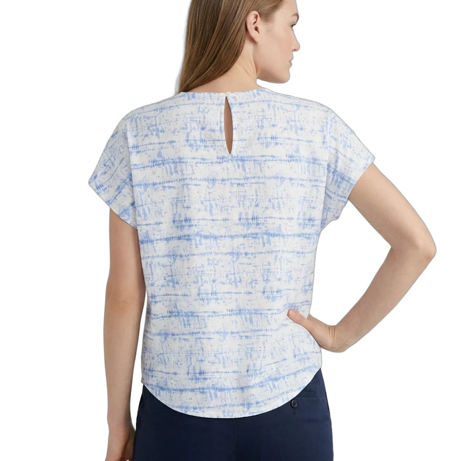 A woman shown from the back wearing a short-sleeve top with a light blue and white abstract pattern and a small keyhole cutout at the back neckline, paired with dark navy pants, against a plain white background.