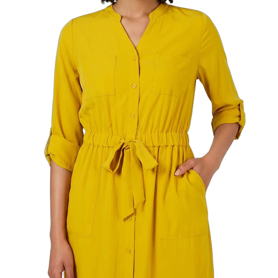 A woman wearing a mustard yellow button-front shirt dress with a tie waist and rolled sleeves, shown against a plain white background.