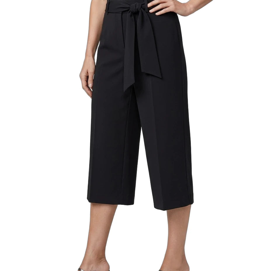 A model wearing black wide-leg cropped trousers with a matching waist tie, paired with a white top and black mule heels, shown against a plain white background.