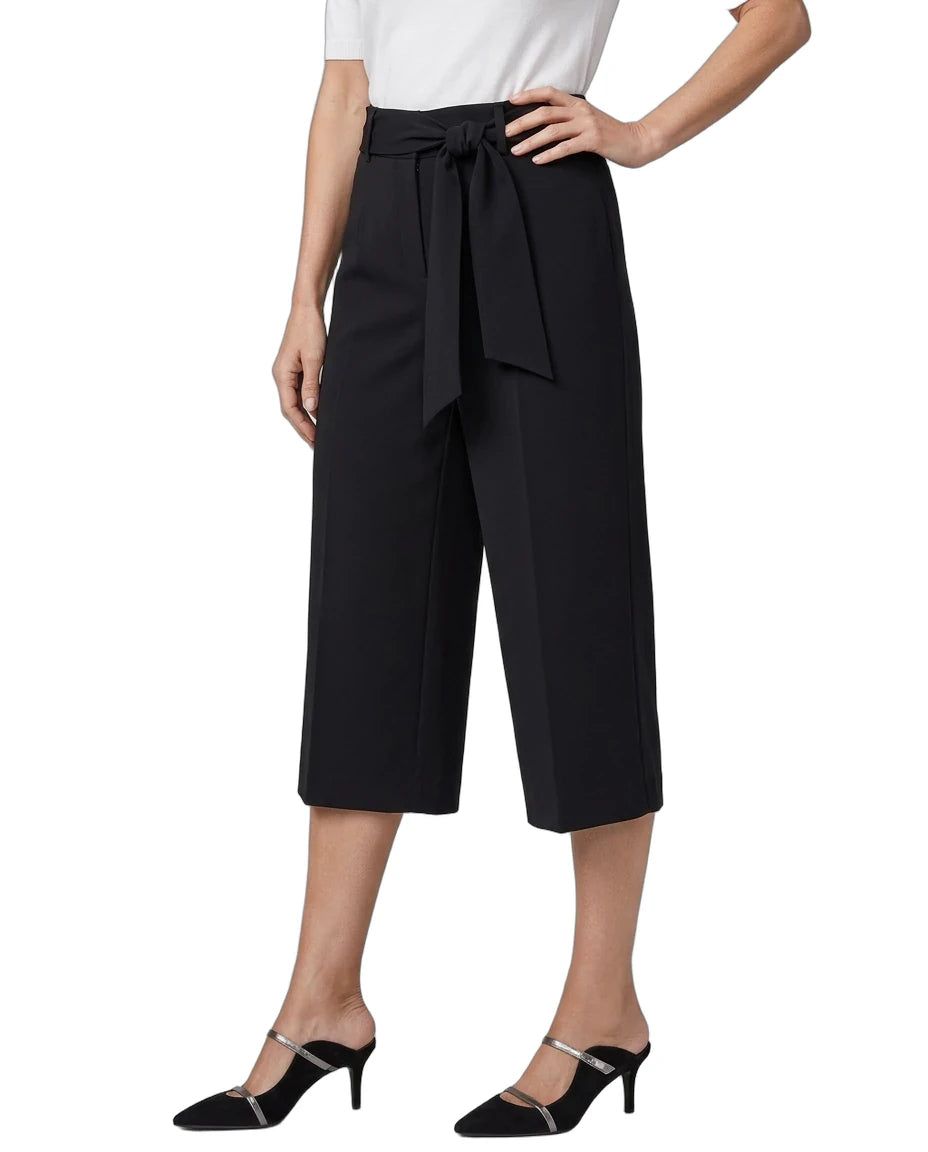 A model wearing black wide-leg cropped trousers with a matching waist tie, paired with a white top and black mule heels, shown against a plain white background.