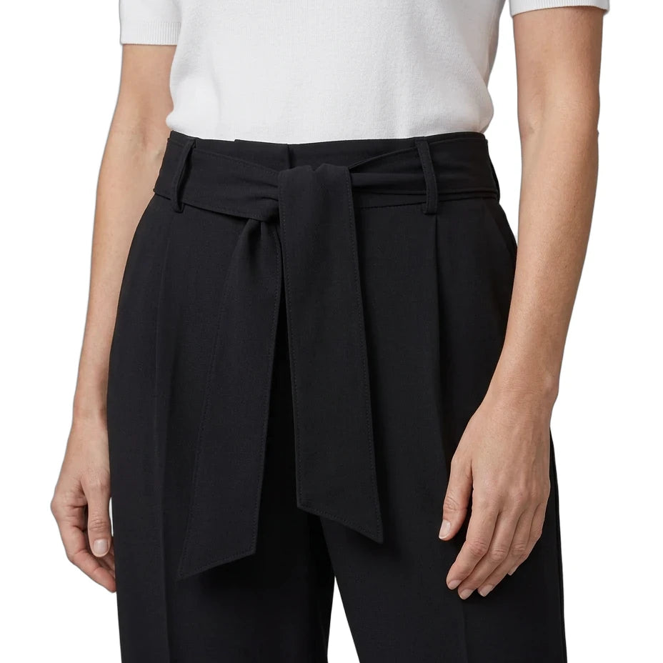 A model wearing black wide-leg trousers with a matching self-tie belt, paired with a white short-sleeve top, shown from the chest down on a white studio background.