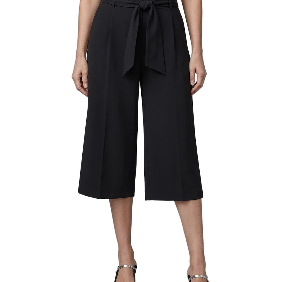 A model wearing black wide-leg cropped trousers with a matching waist tie, paired with a white top and black pointed-toe heels with silver straps, shown against a plain white background.