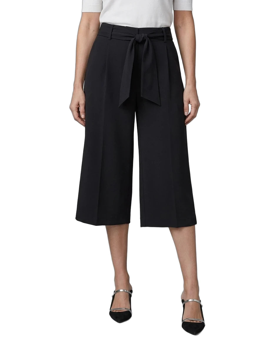 A model wearing black wide-leg cropped trousers with a matching waist tie, paired with a white top and black pointed-toe heels with silver straps, shown against a plain white background.