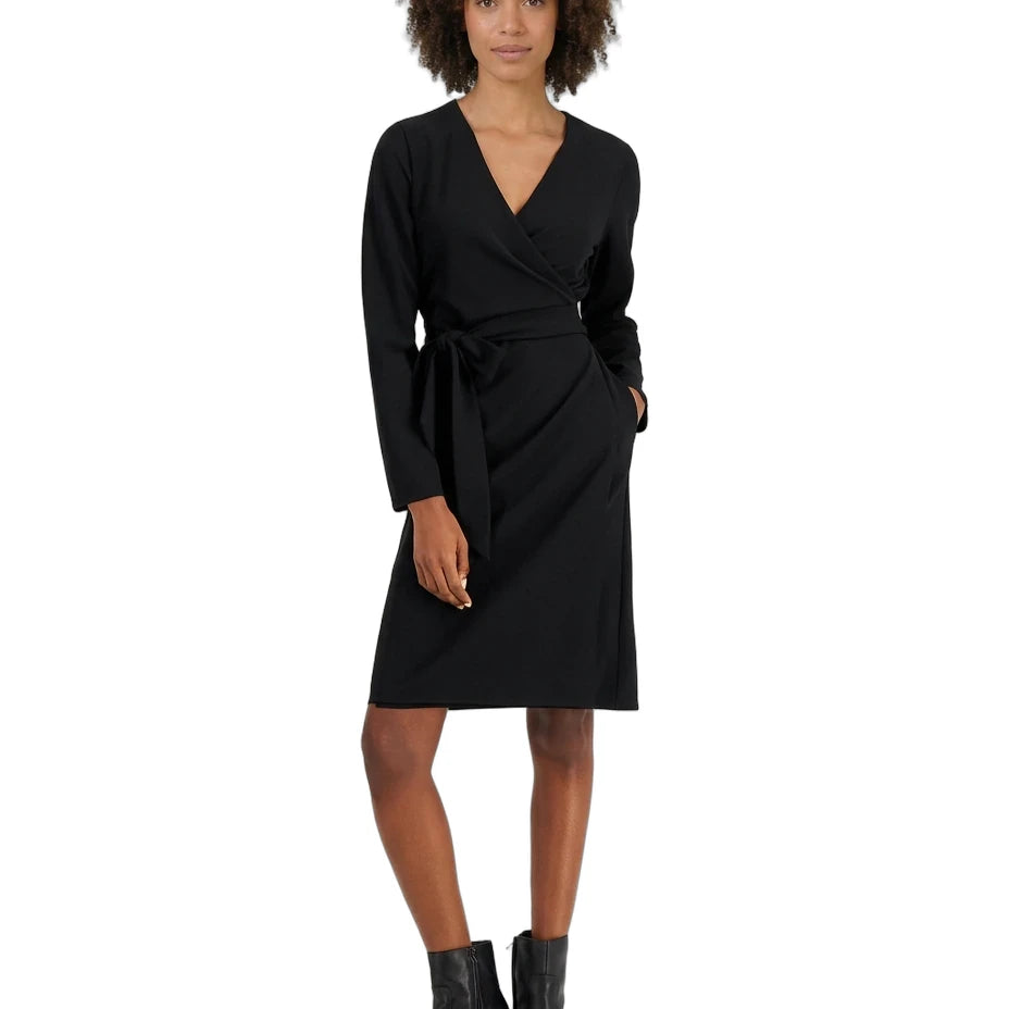 A woman modeling a black long-sleeve wrap dress with a matching waist tie, paired with black ankle boots, against a plain white background.