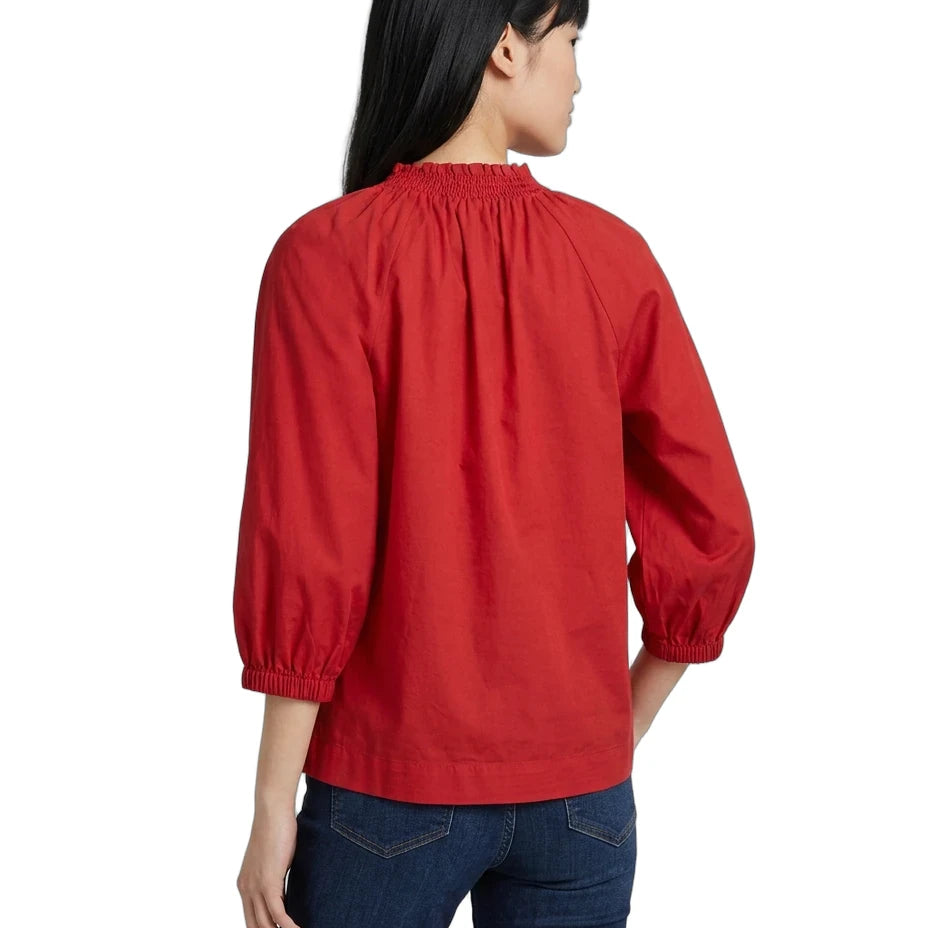 A woman shown from the back wearing a bright red long-sleeve blouse with a gathered elastic neckline and elastic cuffs, paired with dark blue jeans, against a plain white background.