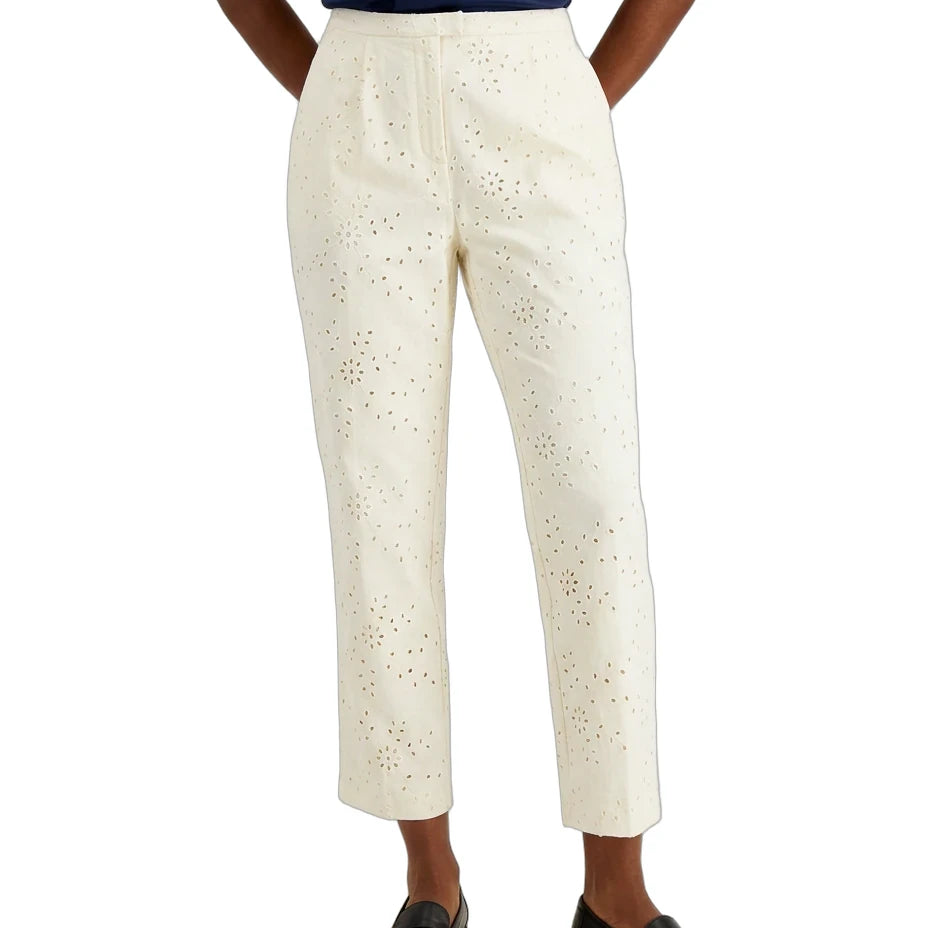 A model wearing off-white cropped trousers with an eyelet cutout pattern, paired with a navy top and black loafers, shown from the waist down on a white background.