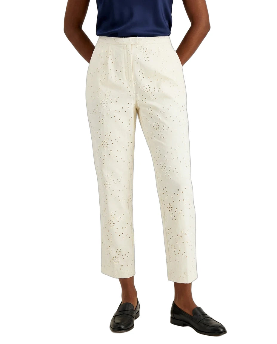 A model wearing off-white cropped trousers with an eyelet cutout pattern, paired with a navy top and black loafers, shown from the waist down on a white background.