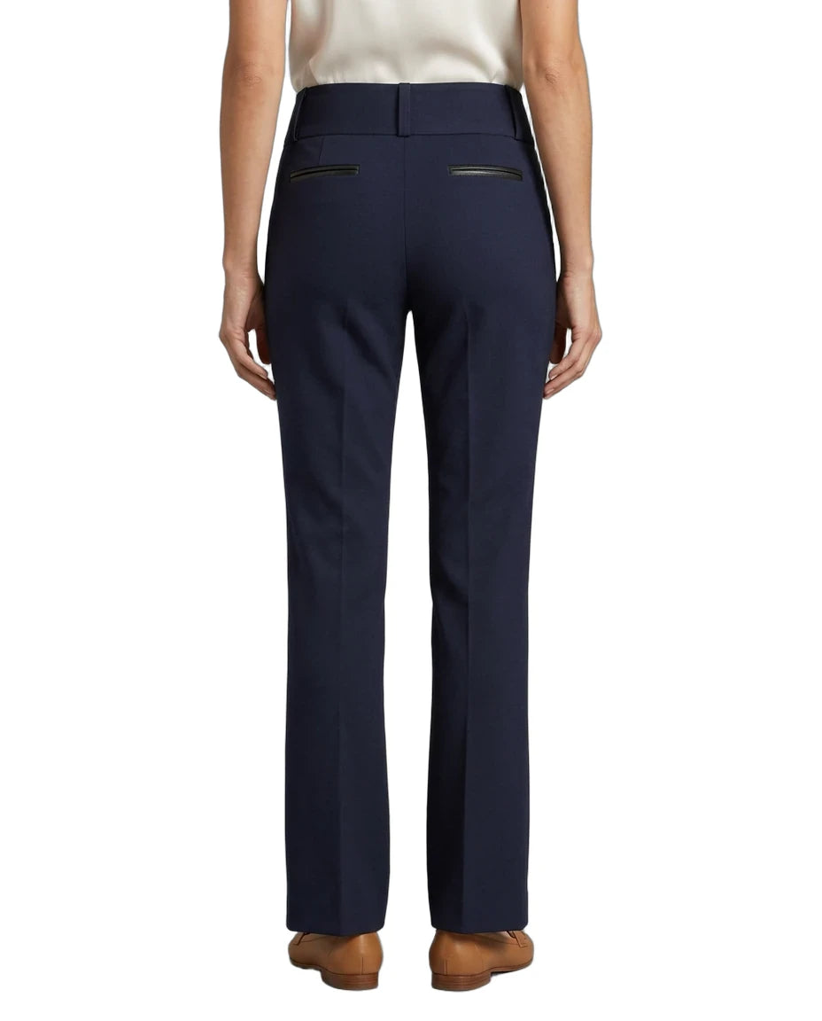 A person shown from the back wearing navy blue straight-leg trousers with zippered back pockets, paired with a light top and brown shoes, against a plain white background.